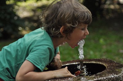 мальчик пьет воду из питьевого фонтана