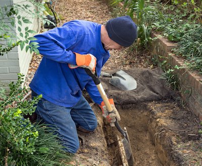 Мужчина копает лопатой траншею для укладки дренажных труб