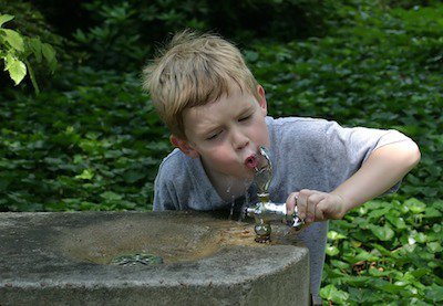 Мальчик пьет воду из уличного фонтана